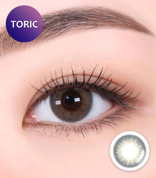 Close-up of an eye wearing Revi Gray toric contact lens, showcasing grayish color with a natural look. Product ID: K013GR, 55% water content.